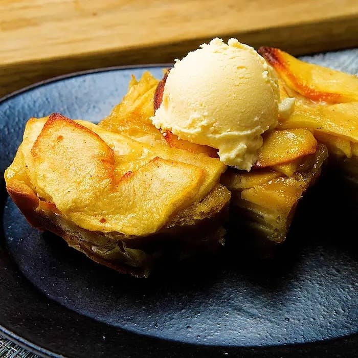 デザートの上にアイスクリームを載せた焼きリンゴのケーキが黒い皿に盛られている。