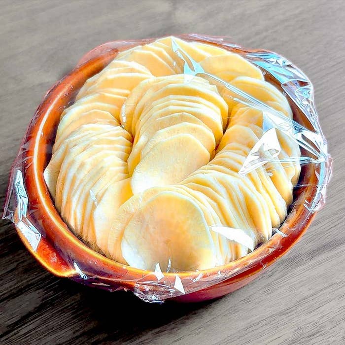 さつまいものスライスが重ねられ、ラップで覆われた陶器のボウルに入っている。
