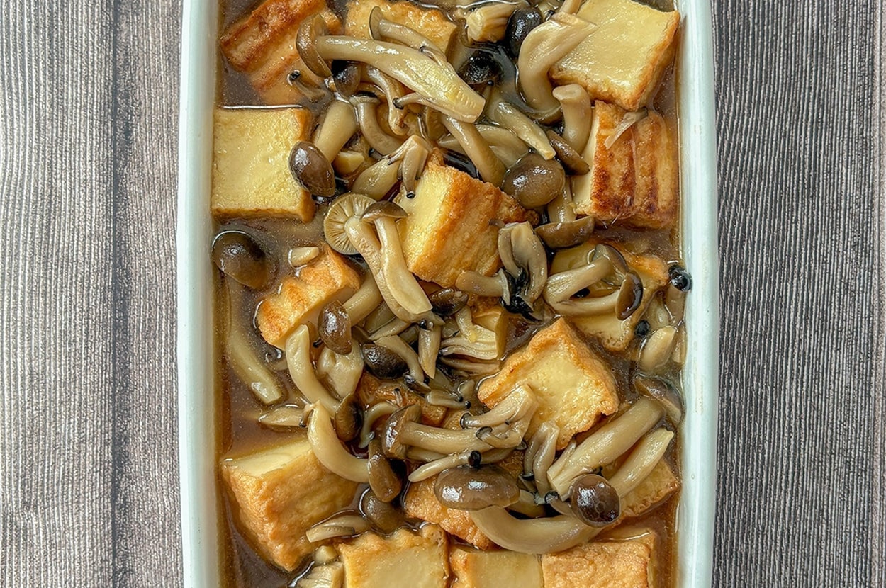 キノコと揚げ豆腐の炒め物が白い皿に盛り付けられた料理。シンプルでヘルシーな一品。