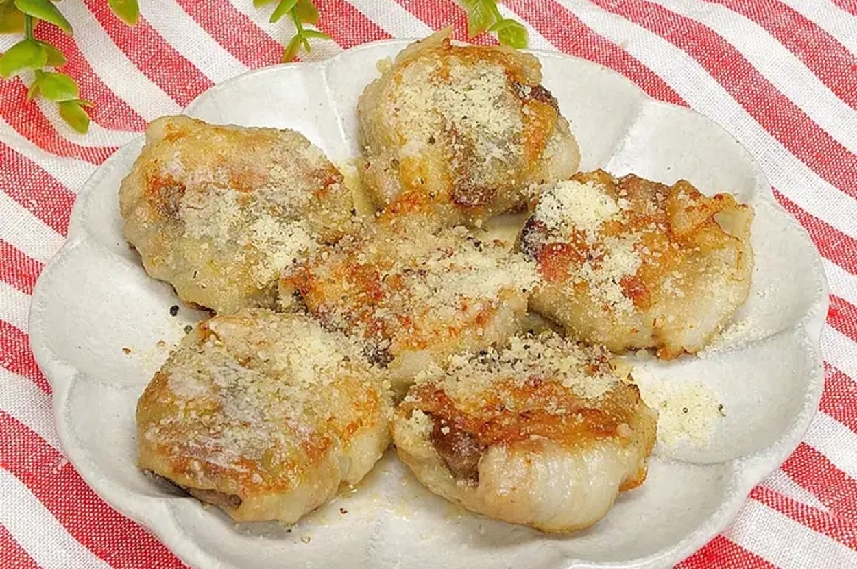 皿に盛られたシュウマイの料理。シュウマイの上にはパウダー状のトッピングがかかっている。背景に緑の植物。