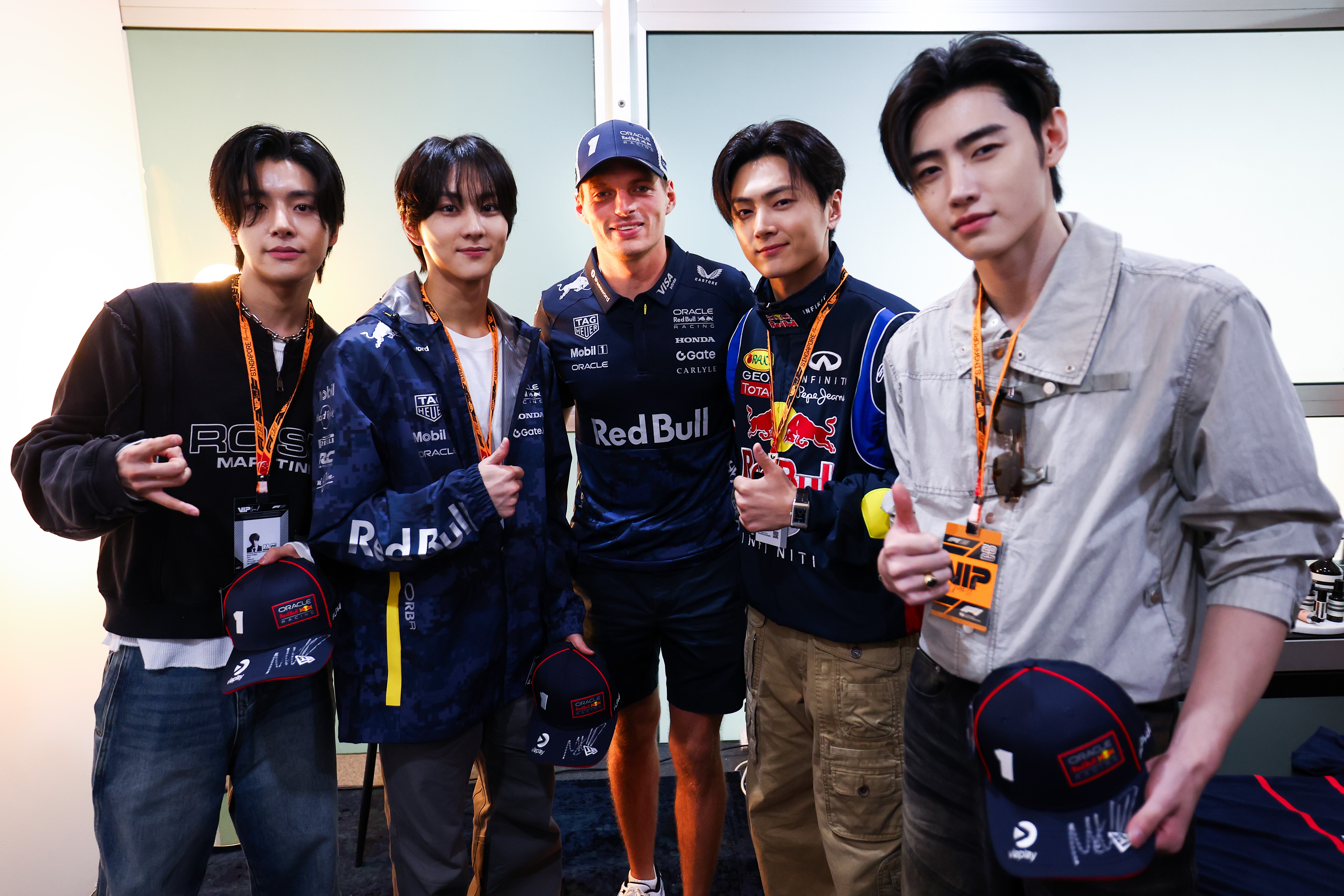 Five people pose together, smiling. The person in the middle wears a racing-themed outfit. Four others hold caps with similar logos