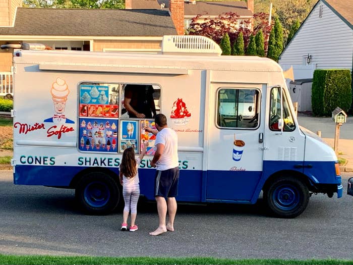 Father and daughter stand at an ice cream truck, deciding on their order