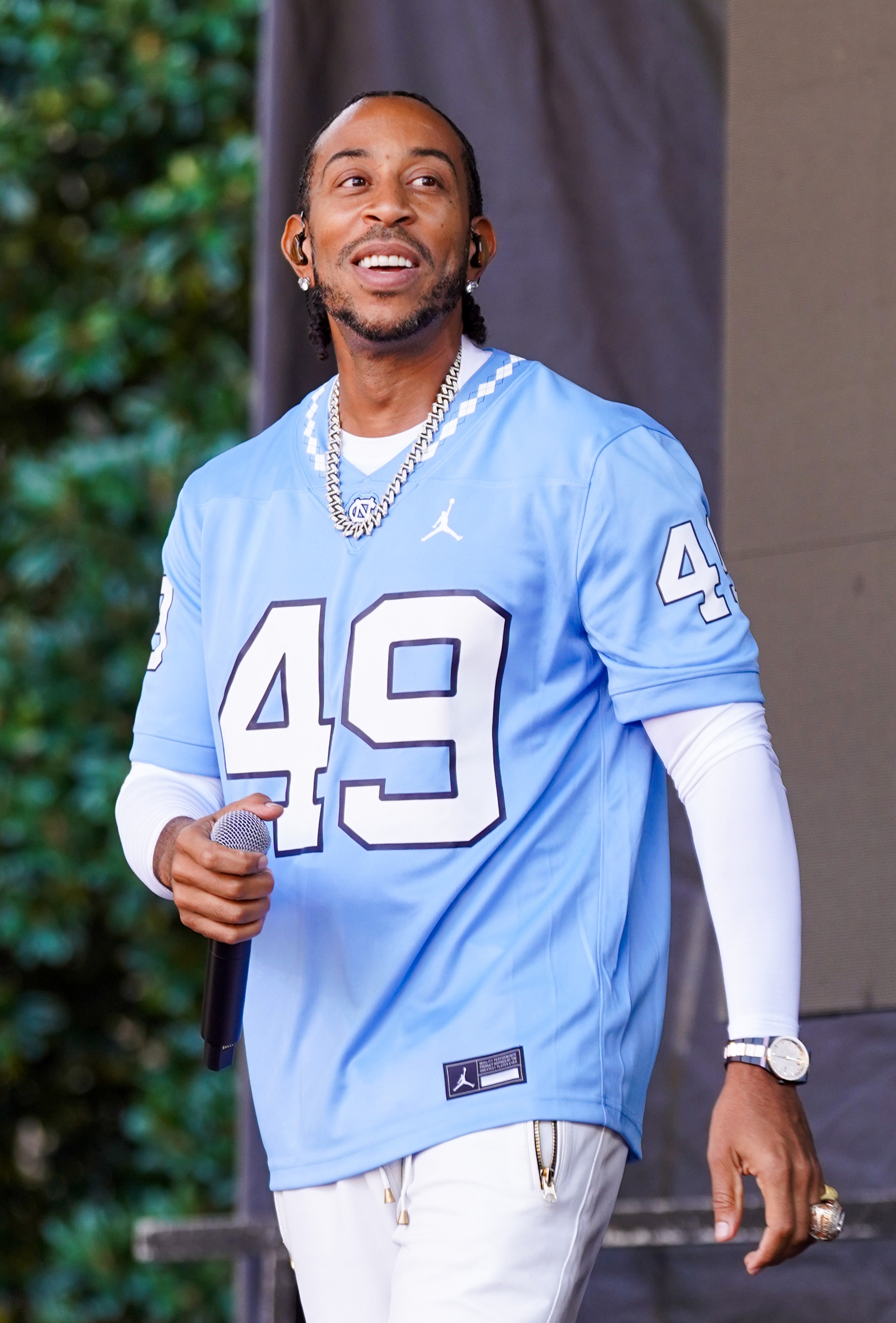 Celebrity wearing a escaped   sports jersey with fig   49, layered implicit    a long-sleeve shirt, holding a microphone, smiling outdoors