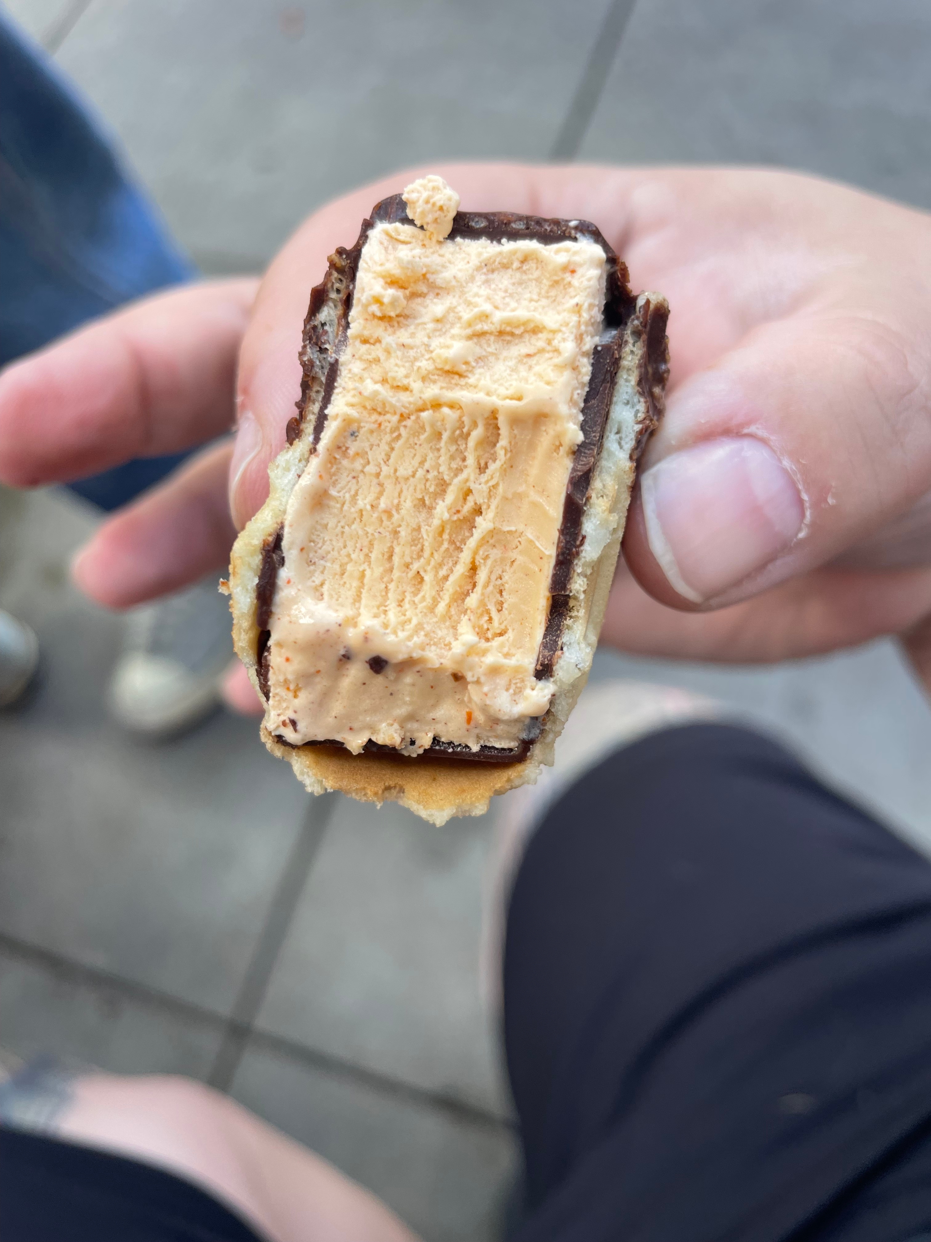 Hand holding a partially eaten ice cream sandwich with chocolate coating and wafer, showing the creamy ice cream filling inside