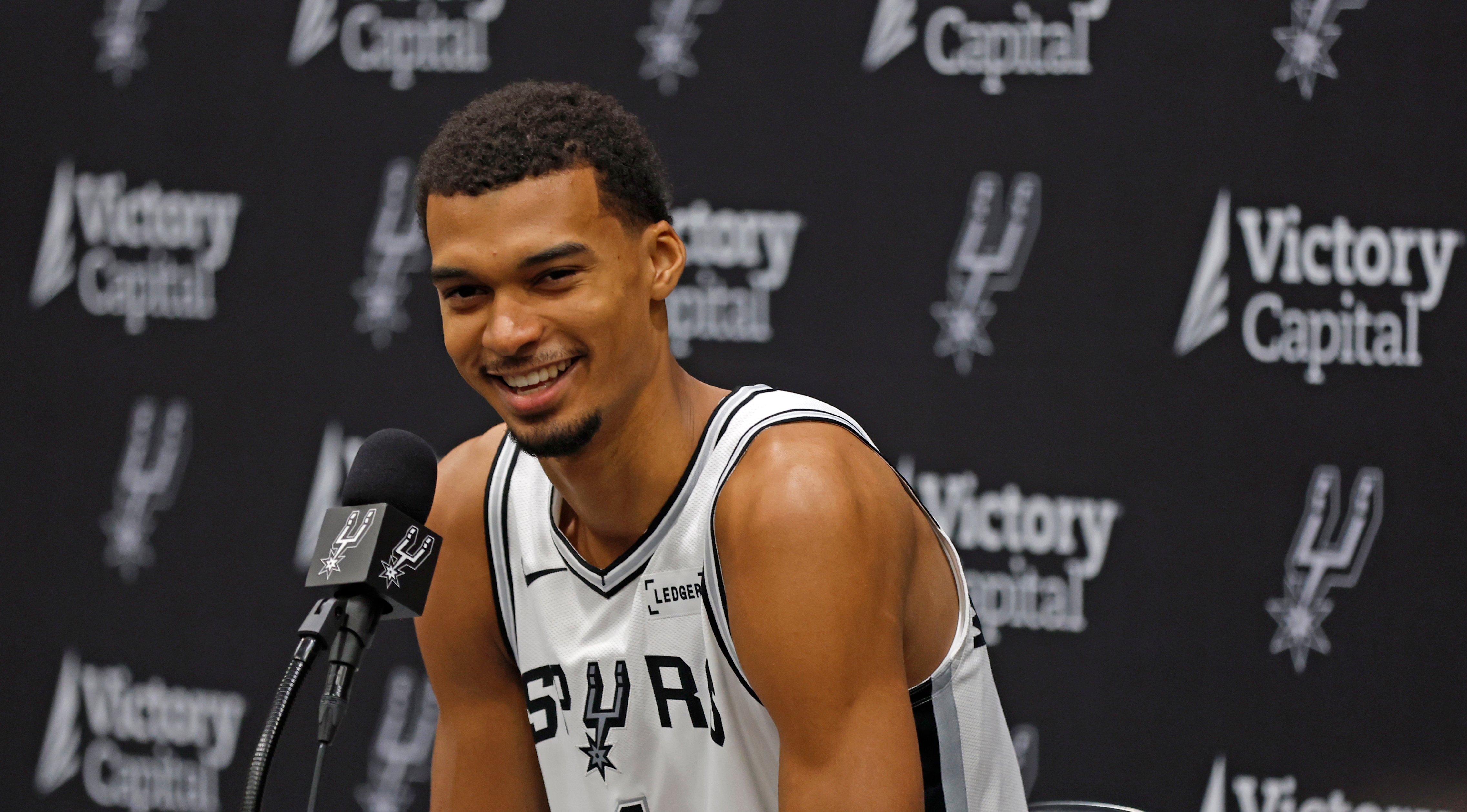 A hoops  subordinate    successful  a Spurs jersey speaks into a microphone astatine  a property   conference