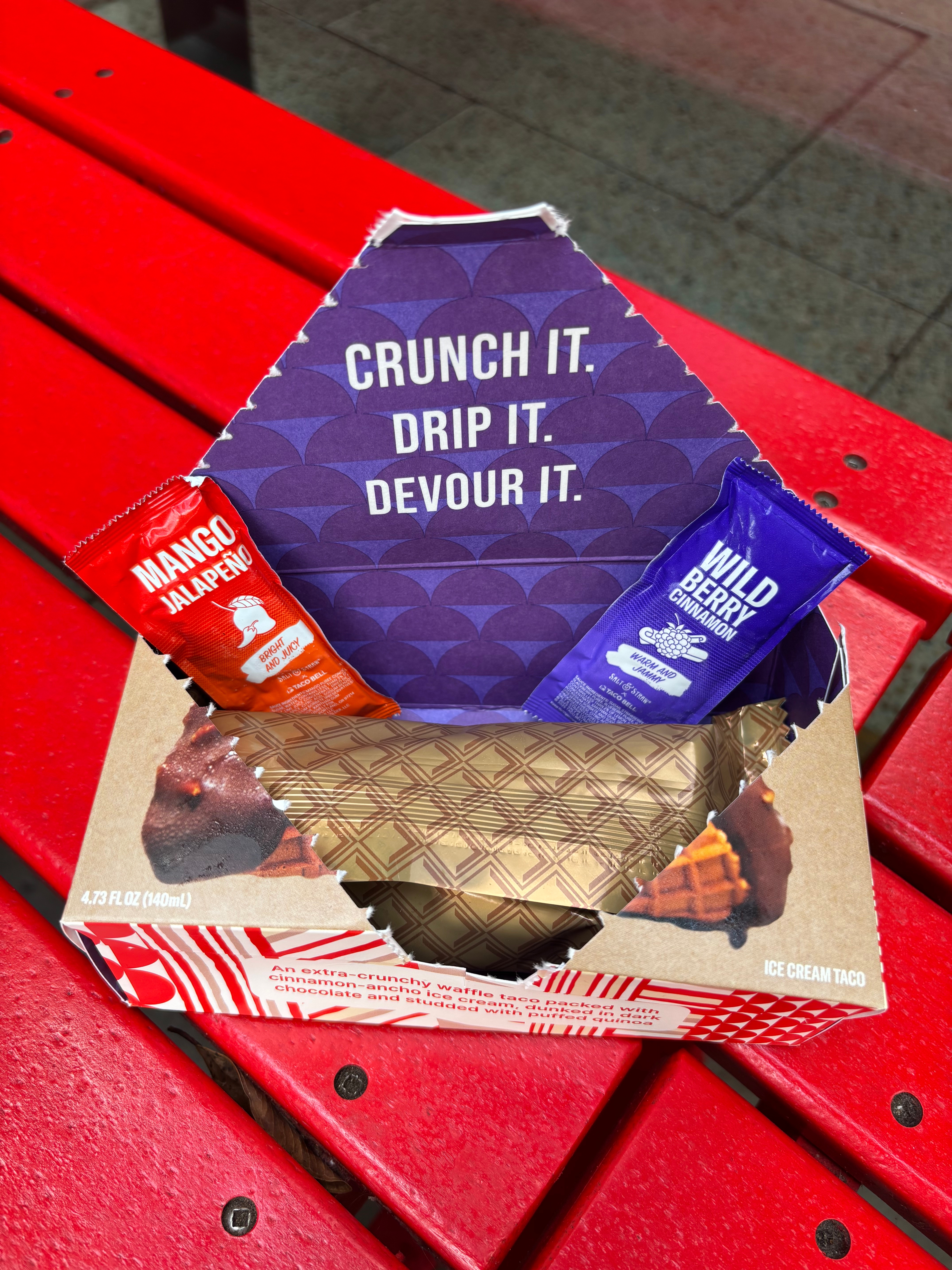 Ice cream taco box on a red bench, open to reveal sauces: mango jalapeño and wild berry. Slogan inside reads, "CRUNCH IT. DRIP IT. DEVOUR IT."