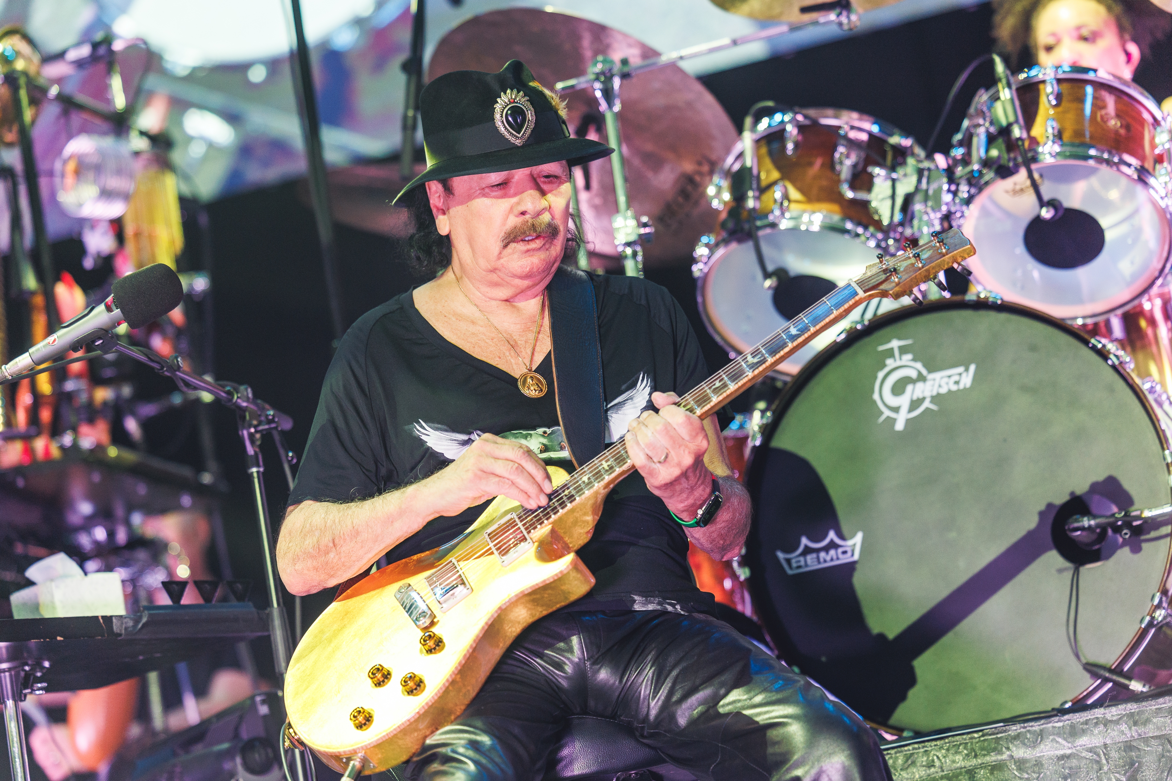 A mustached antheral   connected  signifier    successful  beforehand   of a drumset helium  is wearing a achromatic  chapeau  playing an electrical  guitar