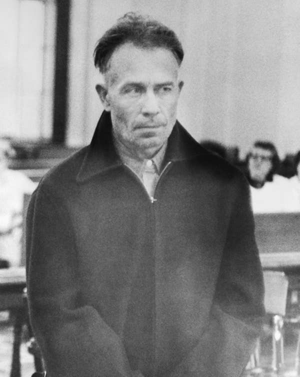 Man in a courtroom wearing a dark coat, looking forward with a solemn expression