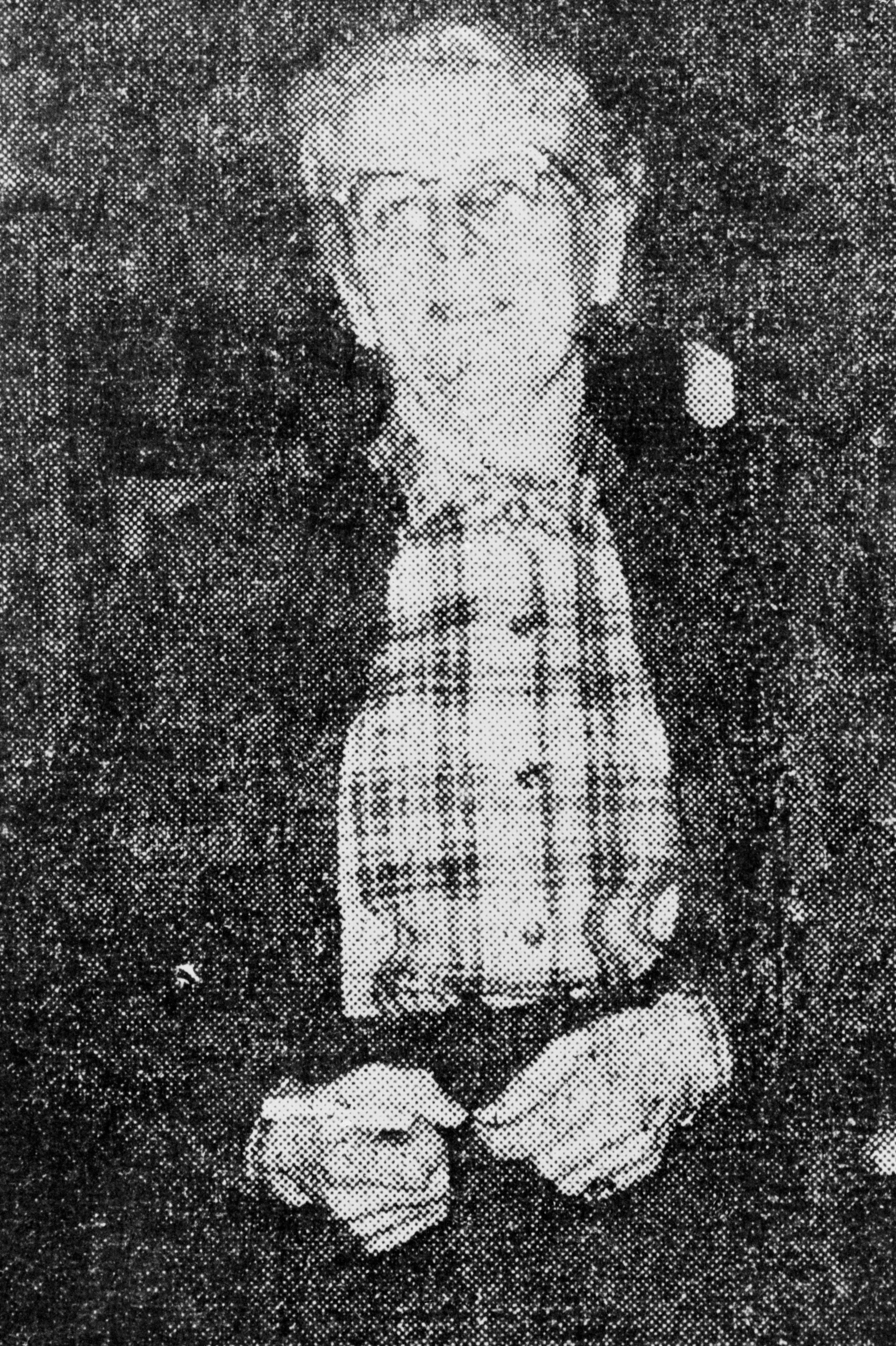 Person in a plaid shirt and jacket, hands clasped, smiling at the camera