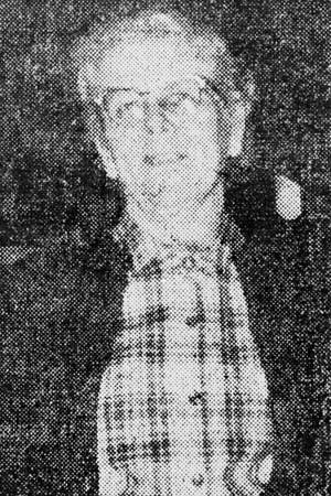 Person in a plaid shirt and jacket, hands clasped, smiling at the camera