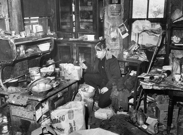 Person examines items in a cluttered, cramped kitchen filled with various containers and papers. The setting appears chaotic and disorganized
