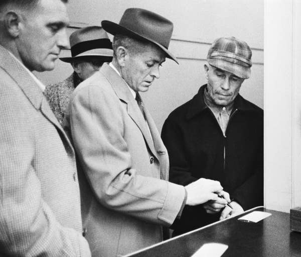 Three men in hats stand together, one opens a cash register. Scene suggests a historical or detective context