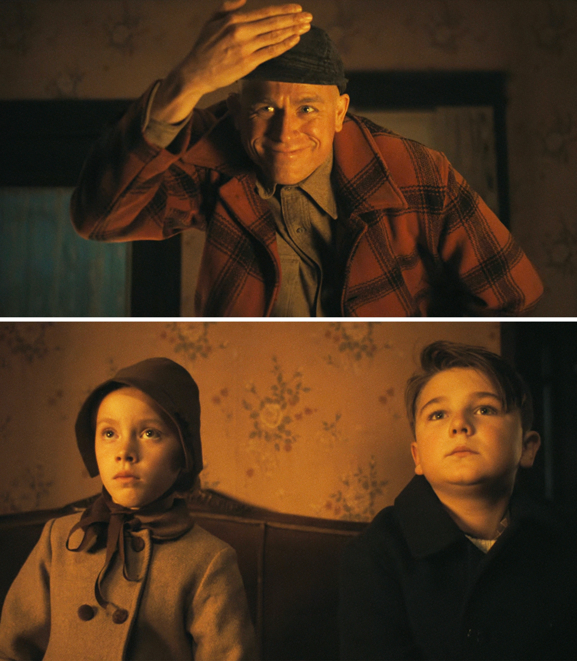 Un uomo più grande punta il cappello, sorridendo calorosamente, mentre due bambini in abbigliamento d'epoca si siedono su un divano, guardando avanti