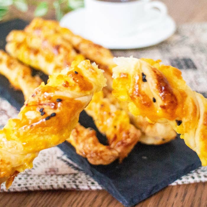 焼きたてのツイストペストリーがプレートに並んでおり、背景にコーヒーカップがあります。