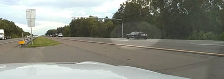 車のダッシュカムから見た、木に囲まれた高速道路。左側にトラック、右側に乗用車が見える。