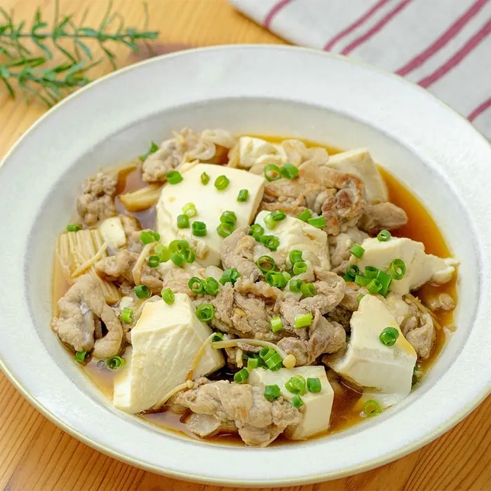 豆腐と薄切り肉の煮込み料理が盛られたお皿。刻みネギがトッピングされています。
