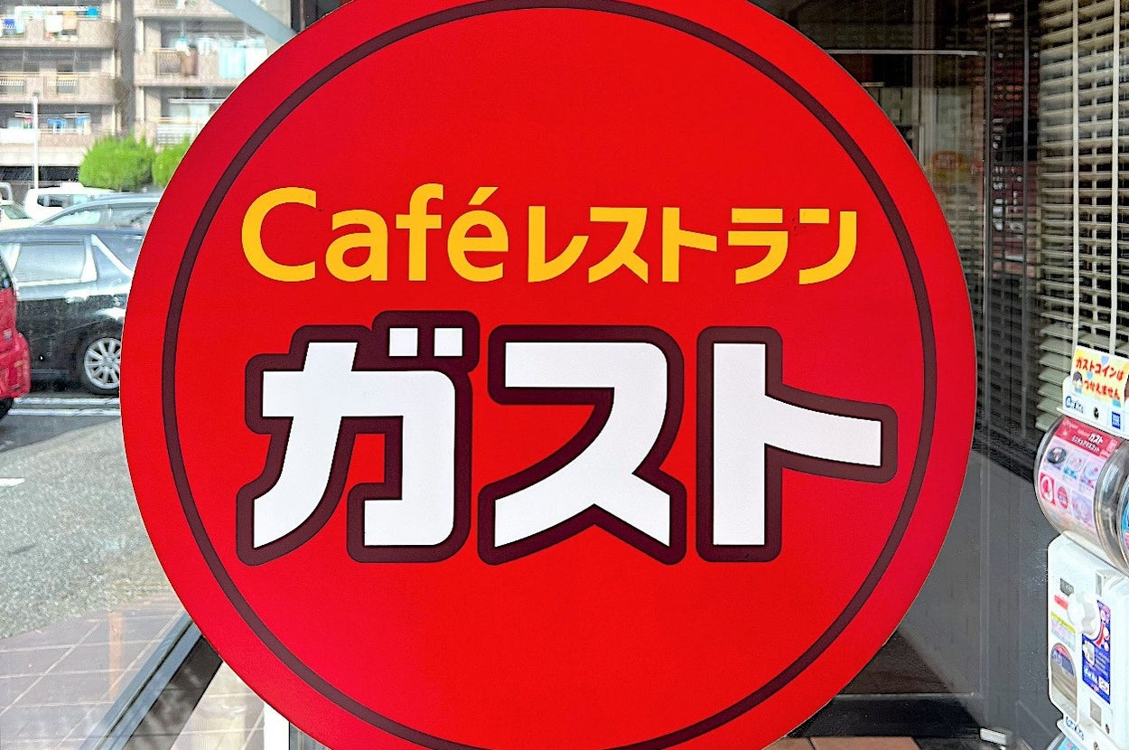 Sign for "Café Restaurant Gusto" on a glass door, visible against a city street backdrop