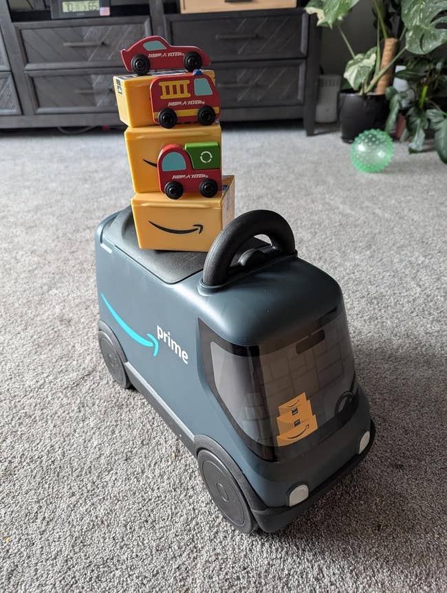 Toy Amazon transportation  motortruck  with a handle, stacked with 3  smaller artifact  bundle  blocks connected  top, placed connected  a carpeted floor