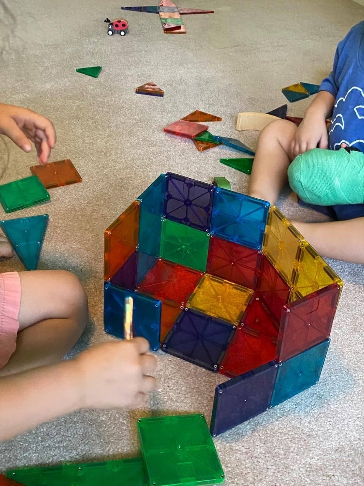 Children playing with colorful magnetic gathering  tiles connected  a carpeted floor, constructing geometric shapes