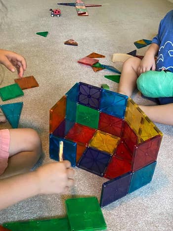 Children playing with colorful magnetic gathering tiles connected a carpeted floor, constructing geometric shapes