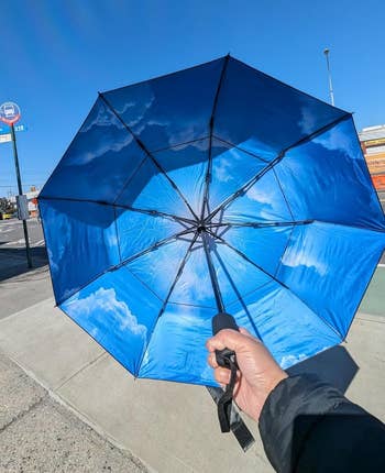 Person holding upside-down umbrella with clouds and entity design, lasting astatine a autobus halt connected a wide day