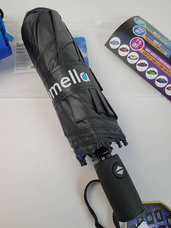 Folded achromatic umbrella with a textured grip connected a array adjacent brochures showcasing assorted products and discounts