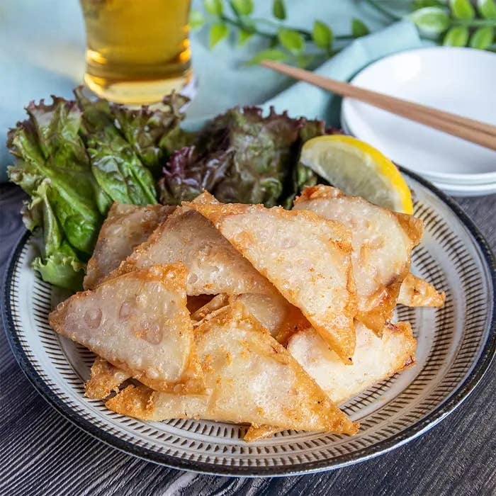 皿に盛られた揚げれんこん料理とレタス、レモン。後ろにビールと箸が置かれている。