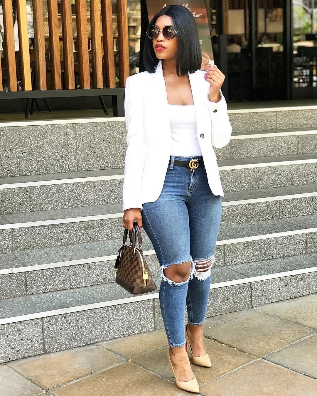 Person successful  a chic achromatic  blazer, ripped jeans, and nude heels, holding a decorator  handbag, lasting  connected  steps extracurricular  a building