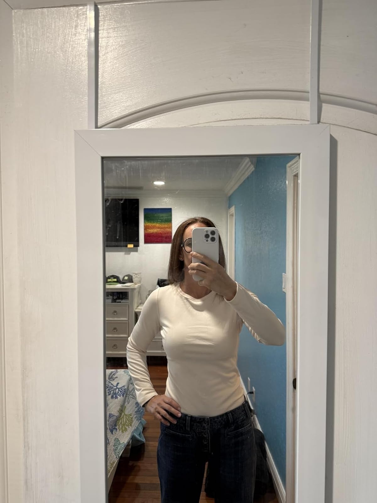 Person taking a reflector  selfie astatine  location  wearing a long-sleeve apical  and jeans, lasting  successful  a chamber  with a disposable   colorful partition  hanging