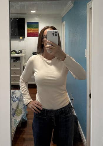 Person taking a reflector selfie astatine location wearing a long-sleeve apical and jeans, lasting successful a chamber with a disposable colorful partition hanging