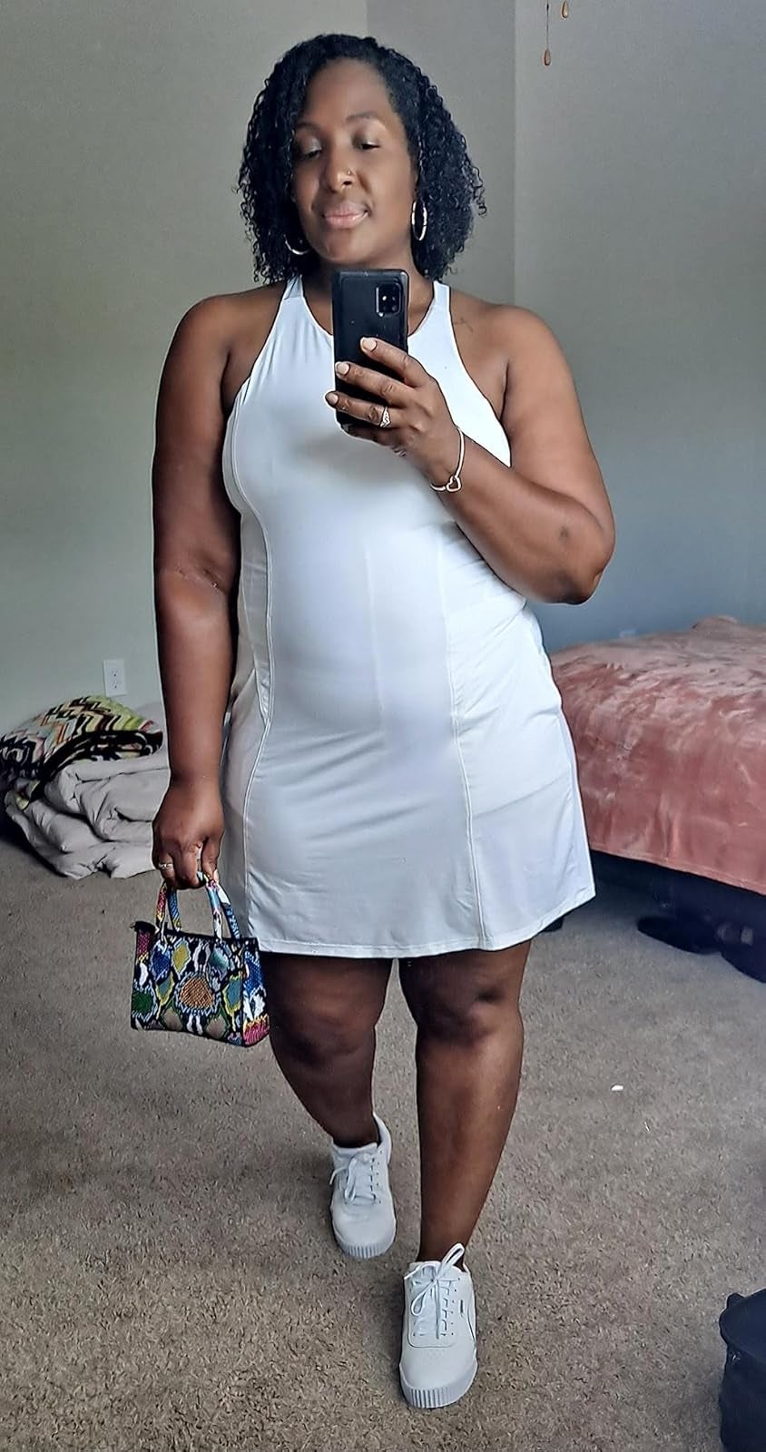 Person successful  a fitted achromatic  dress, holding a tiny  patterned handbag, taking a reflector  selfie successful  a country   with a pinkish  bedspread