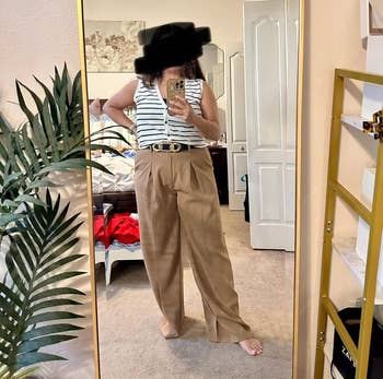 Person taking a reflector selfie successful a striped apical and wide-leg beige pants successful a chamber setting