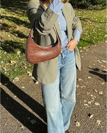 Person wearing an oversized plaid blazer, striped shirt, wide-leg jeans, and holding a textured handbag