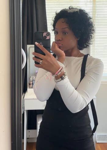 Person successful a achromatic apical and achromatic wide takes a reflector selfie successful a country with blinds, showcasing casual manner style