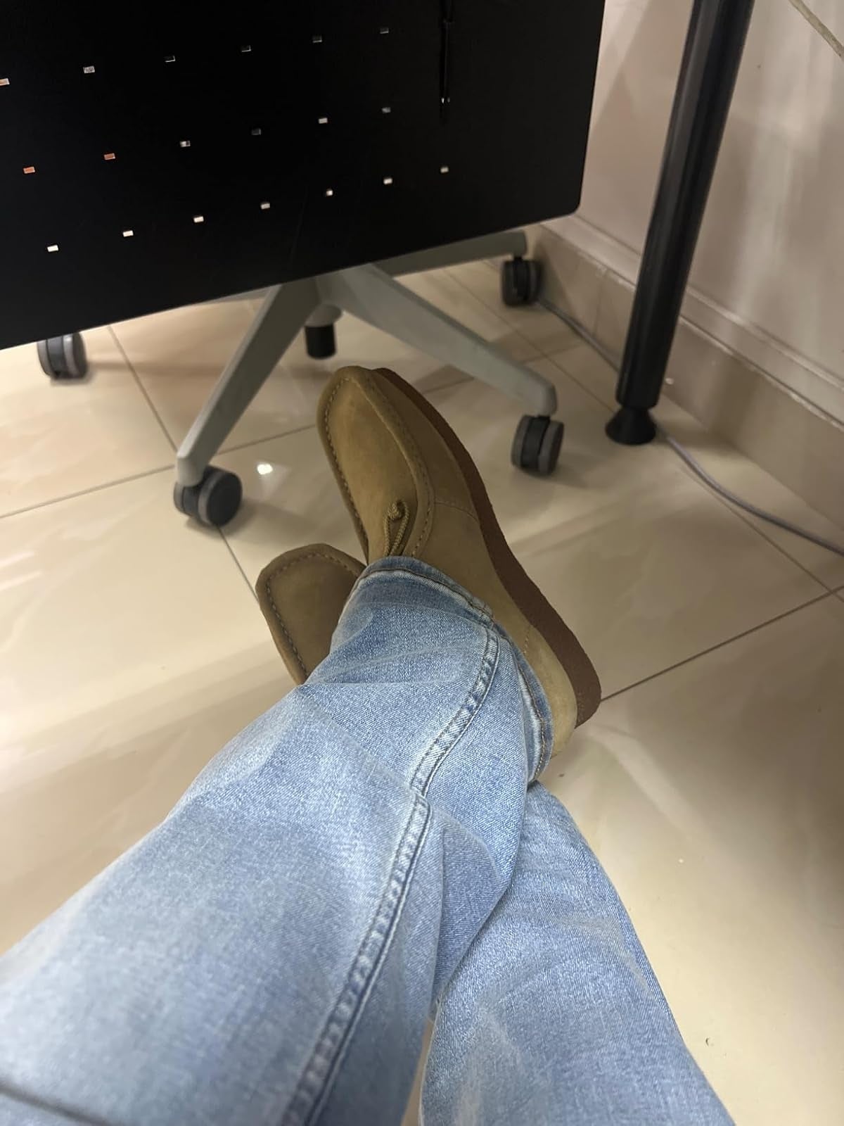 Person wearing airy  jeans and beige loafers, sitting with legs crossed nether  a desk