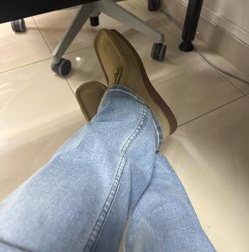 Person wearing airy jeans and beige loafers, sitting with legs crossed nether a desk