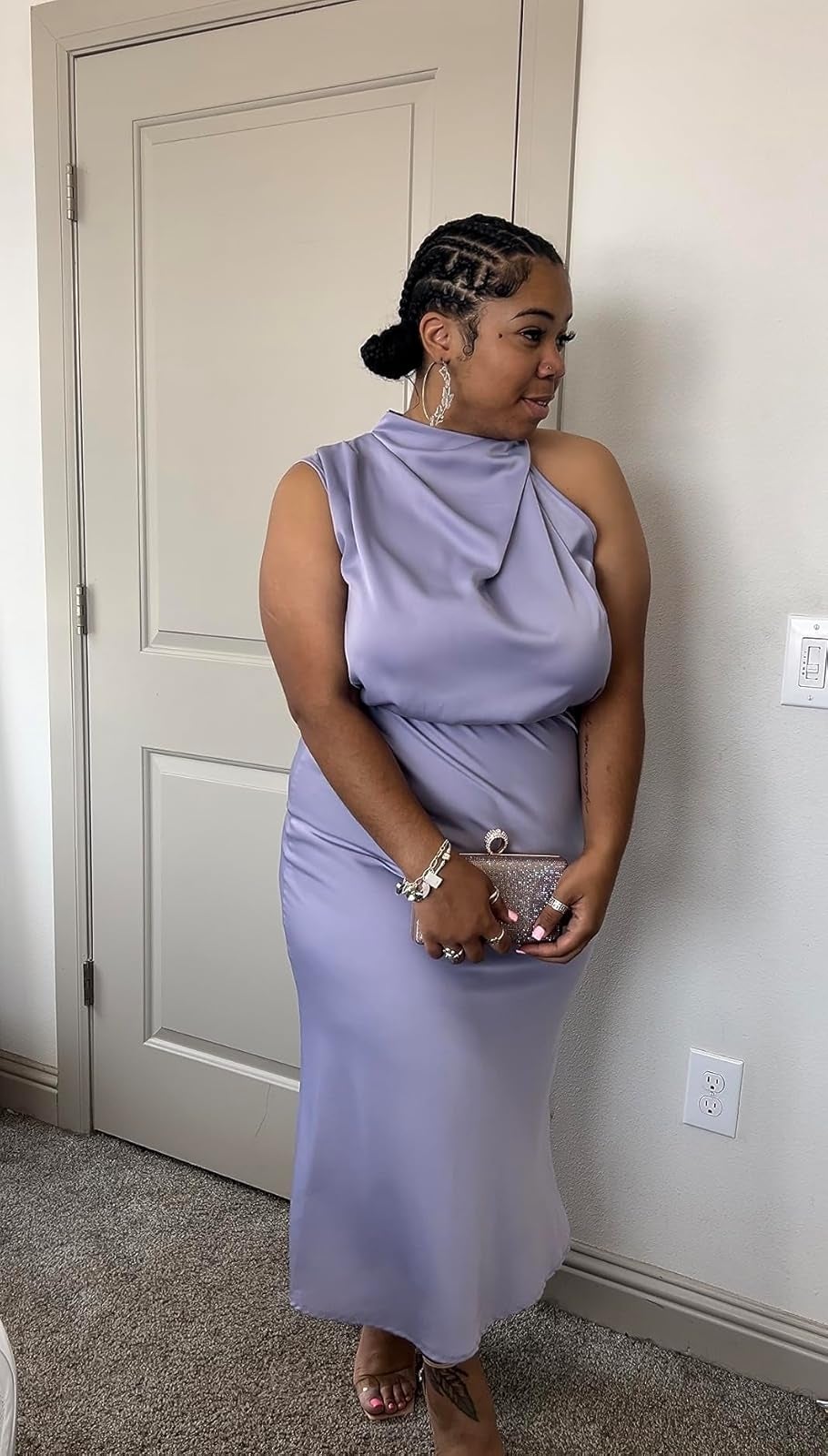 Person successful  elegant sleeveless gown, holding a clutch, stands indoors. Hair styled up   with accessories. Fashion focus