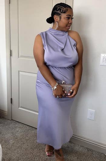 Person successful elegant sleeveless gown, holding a clutch, stands indoors. Hair styled up with accessories. Fashion focus