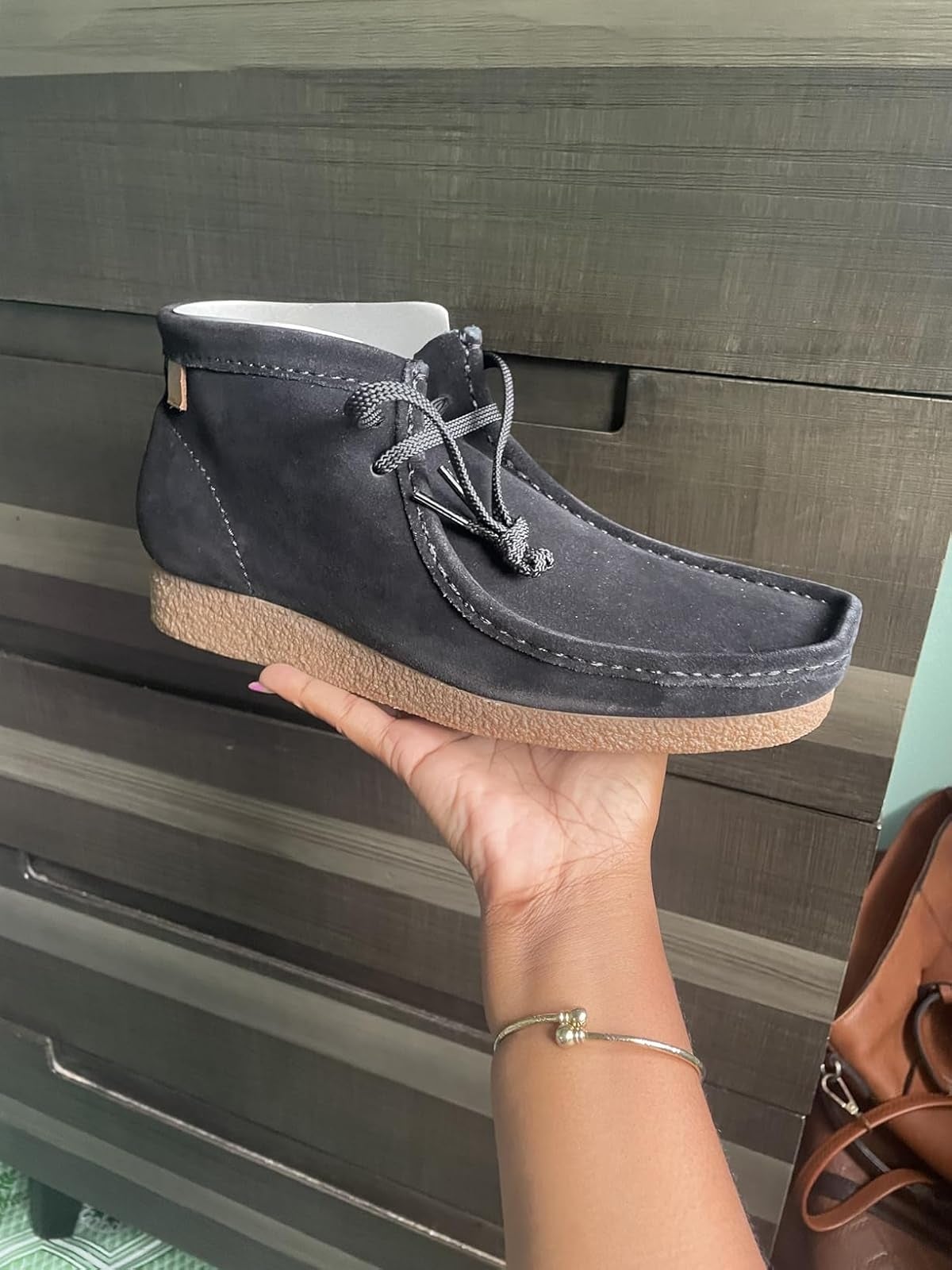 Hand holding a stylish suede ankle footwear  with a rubber sole, against a woody  background