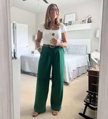 Person successful a chamber reflector selfie, wearing a achromatic apical and wide-legged greenish pants, smiling and holding a smartphone