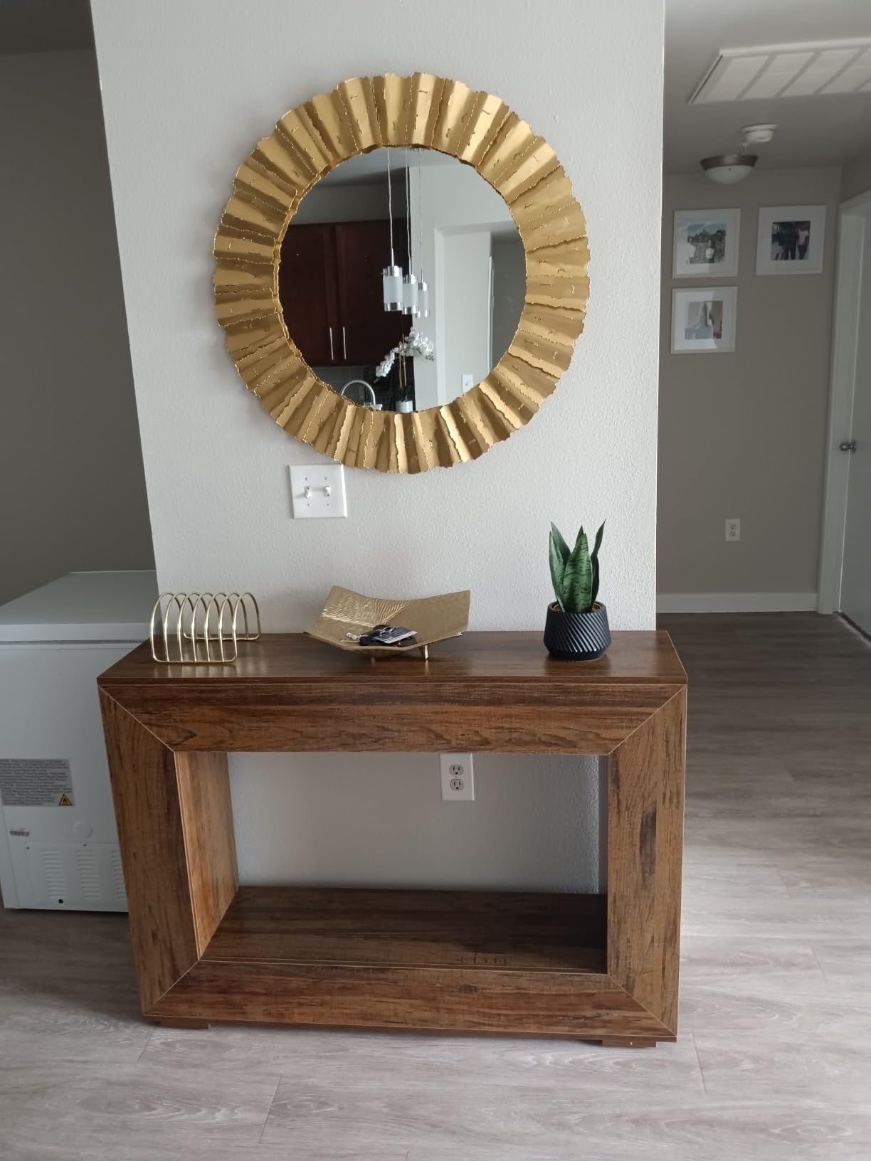 Stylish entryway with a woody  console table, decorative golden  mirror, tiny  plant, and decorative items displayed connected  the tabletop