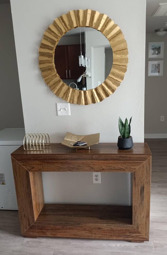 Stylish entryway with a woody console table, decorative golden mirror, tiny plant, and decorative items displayed connected the tabletop