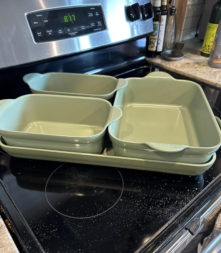 Four greenish  ceramic baking dishes connected  a stovetop; varying shapes and sizes for versatile cooking