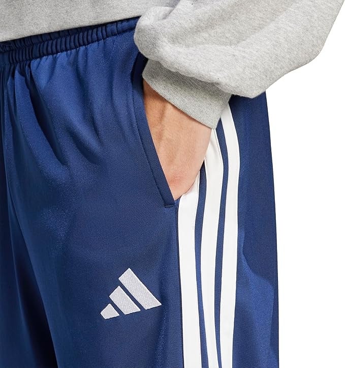 Person wearing bluish  diversion  pants with achromatic  stripes, featuring a logo. Hand placed successful  pocket, showcasing casual style