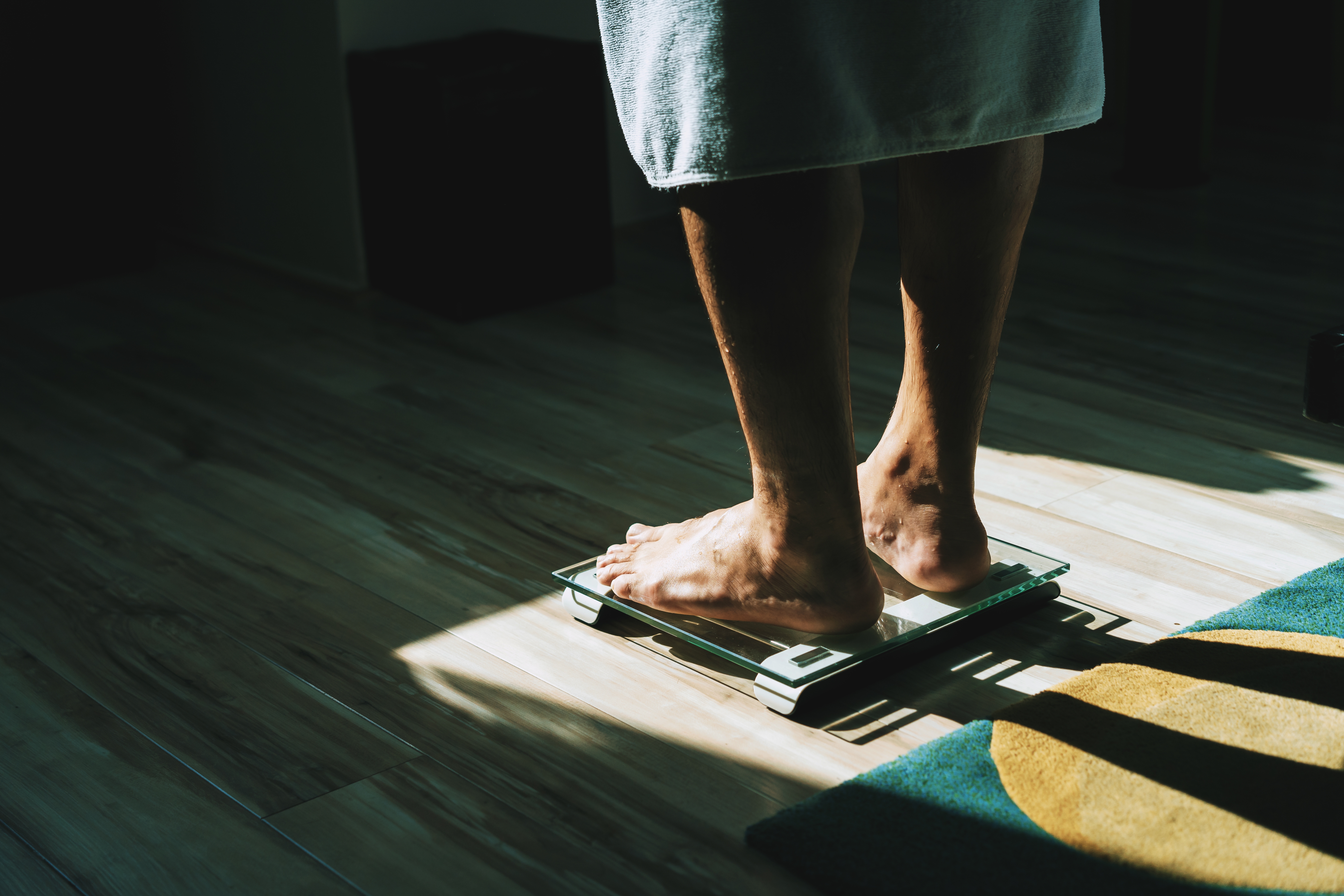Personen som står på en skala på baderomsplass plassert på tregulv, delvis opplyst av sollys