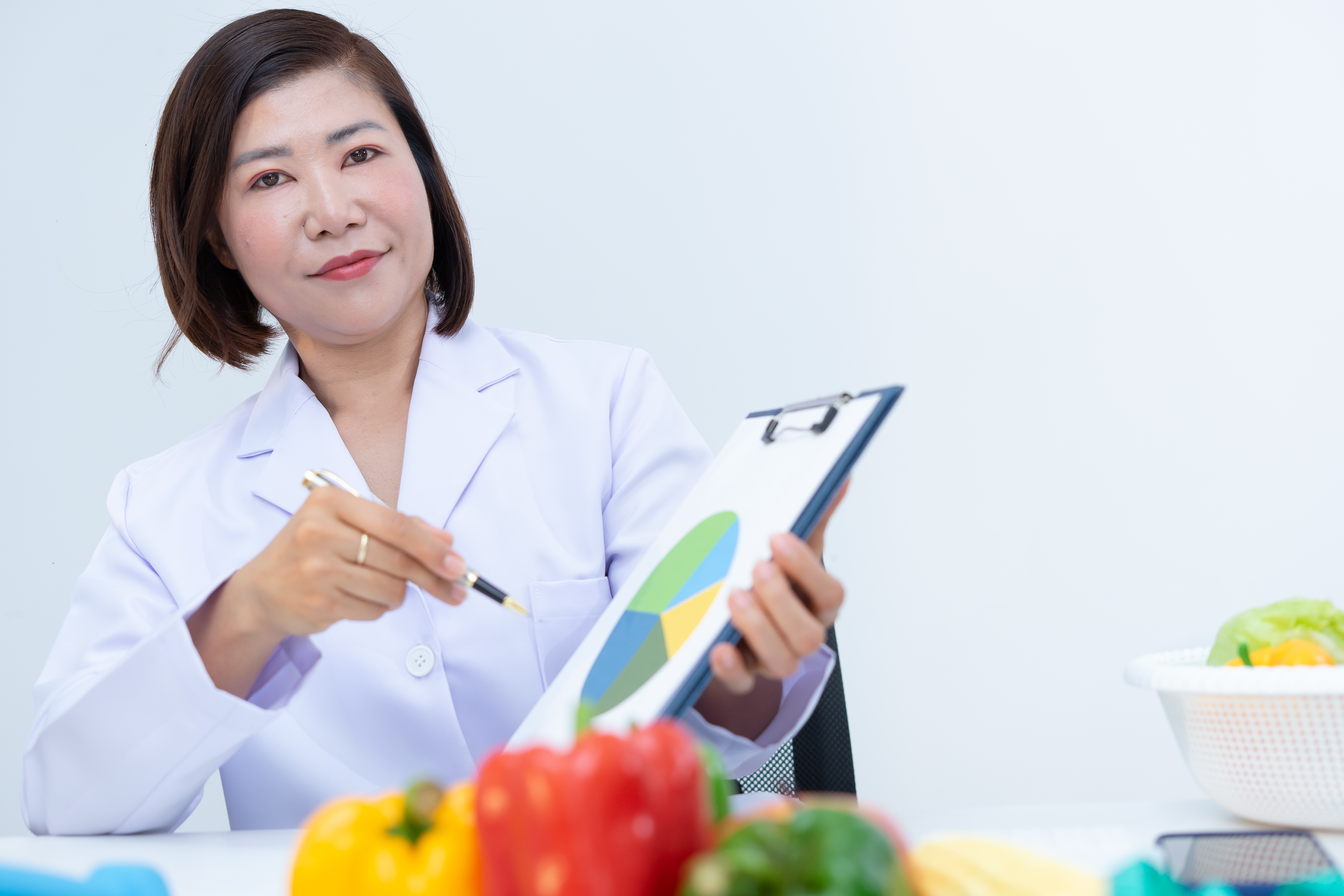 En person i et laboratorium belegg peker på et kakediagram på et utklippstavle, med friske grønnsaker på et bord foran