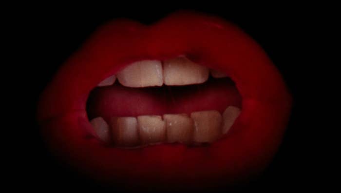 Close-up of lips slightly parted, with visible teeth, set against a dark background