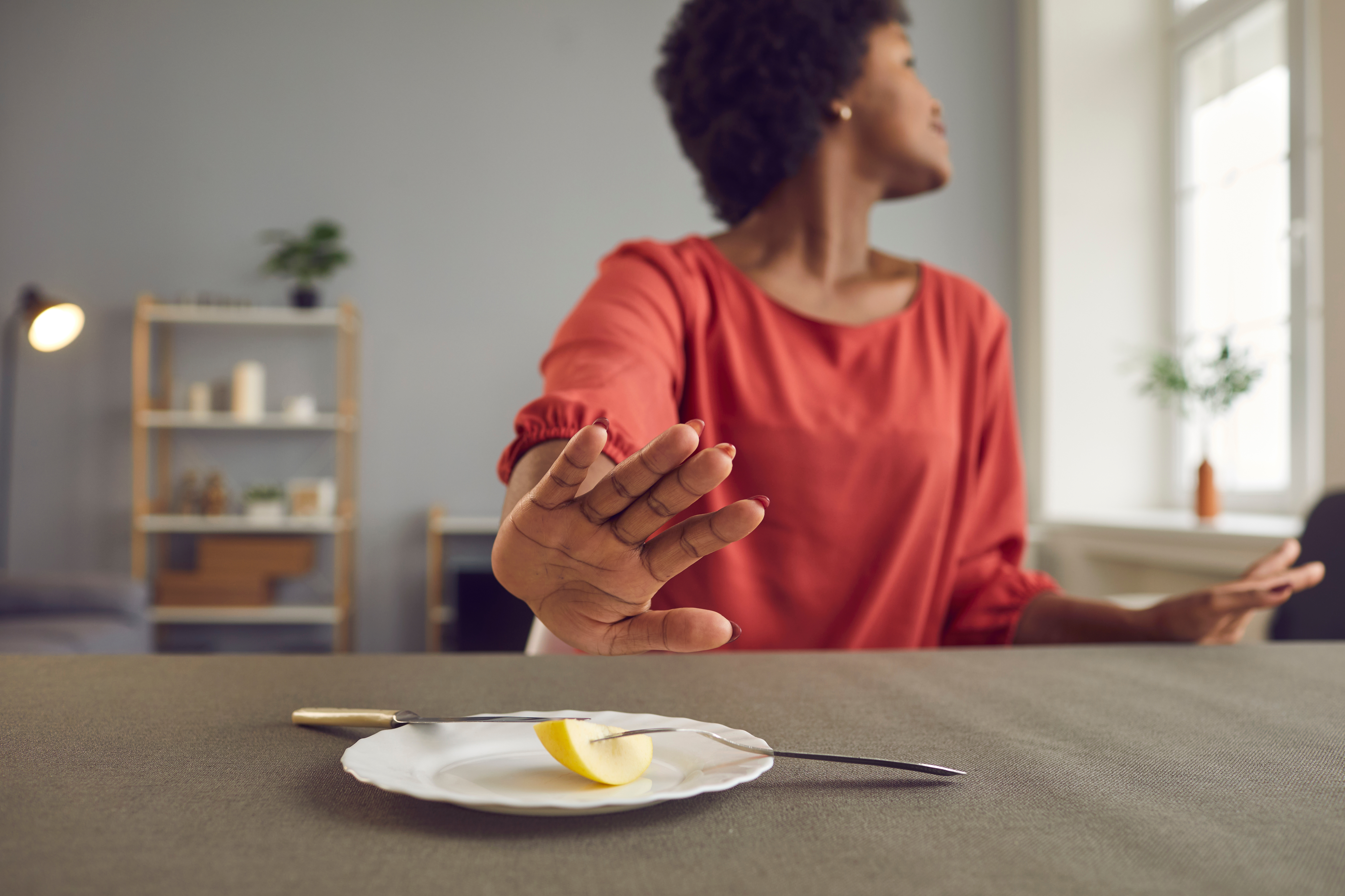 Person i en rød skjorte gester ' stopp ' Mens du sitter ved et bord med et lite stykke mat på en tallerken, ser du bort