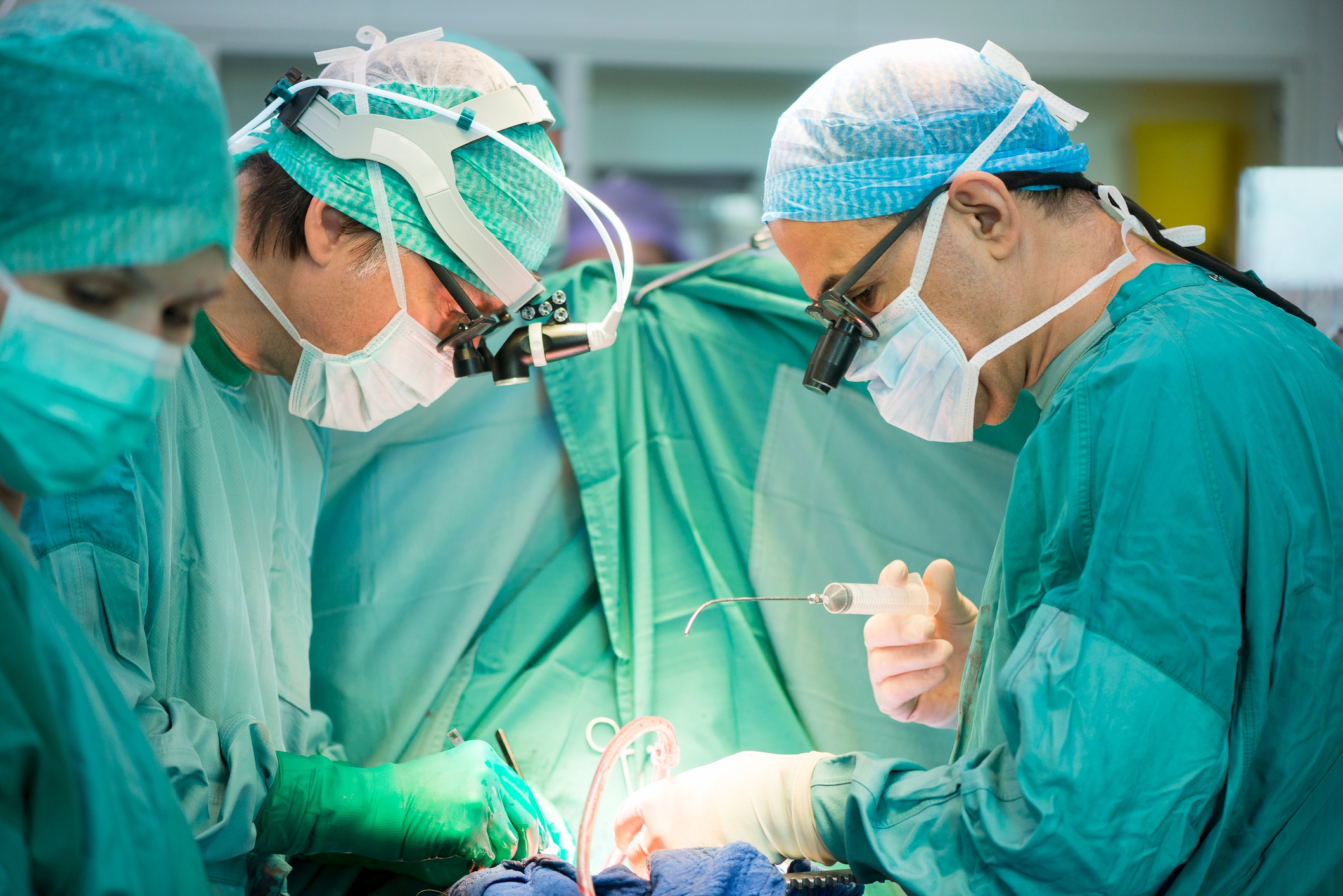 Kirurger i skrubber og masker fokuserer intenst under en operasjon, omgitt av medisinsk utstyr og sterke lys