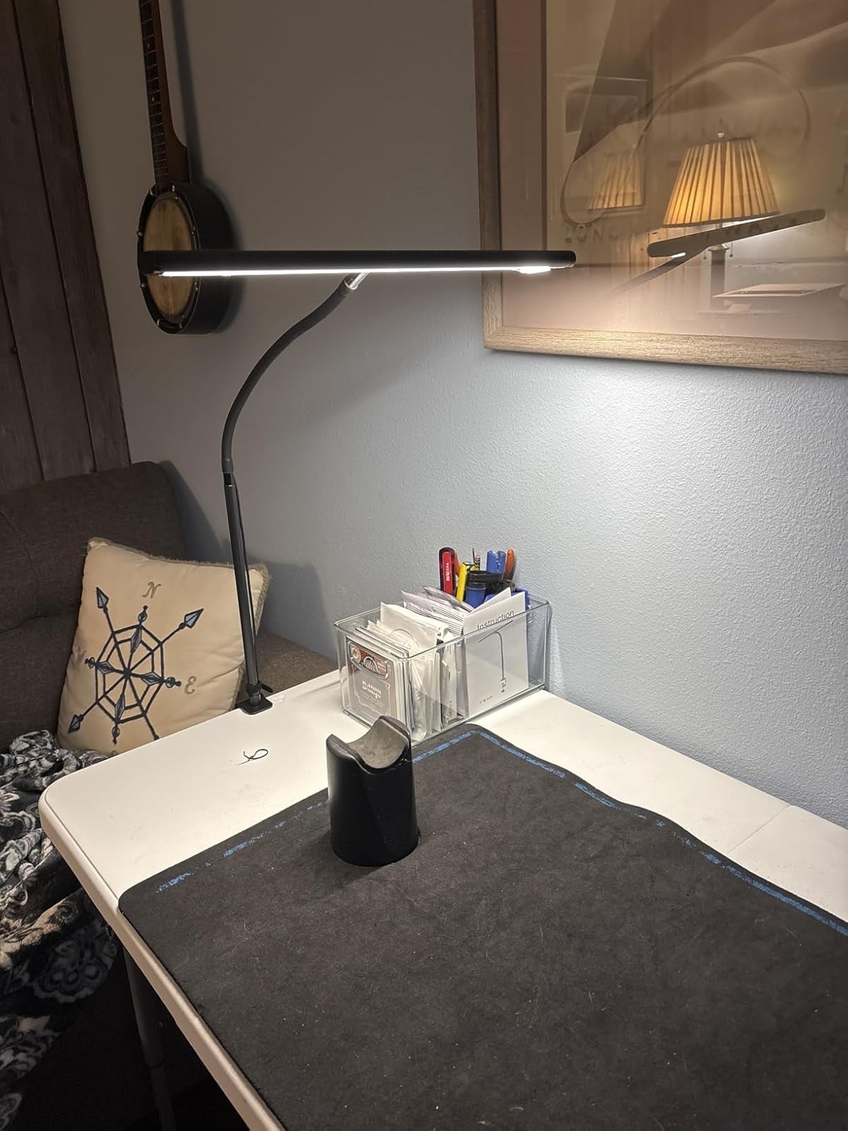 Desk with angled lamp, record  organizer with pens and cards, a pillow with compass design, and a mandolin connected  the wall
